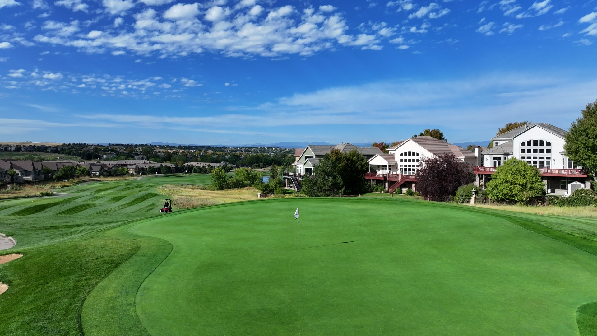 View of flagpole on putting green with houses and sky in background