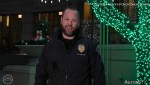 smiling police officer standing next to tree with holiday lights