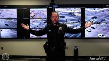 Aurora police officer standing in front of several TV security monitors