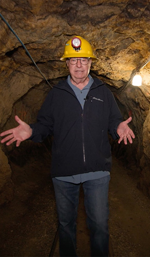 show host walking in mine underground with hard hat on