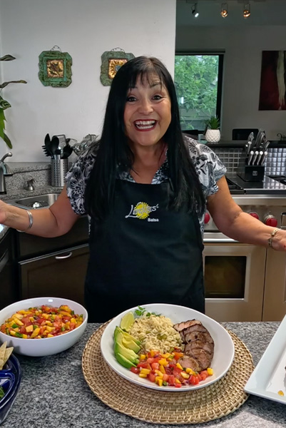 smiling Lindita wearing navy blue apron and showing off finished dish