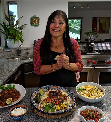 Lindita smiling in her kitchen in front of several plates of Mexican food