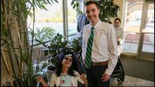 smiling boy wearing tie and standing next to smiling girl in wheelchair wearing dress