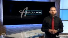 Blaine Robinson standing in AuroraTV studio with Aurora Now graphic in background