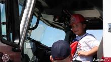 smiling little boy wearing plastic firefighter's hat and sitting in a fire truck