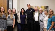 smiling Aurora police officer with members of the family of a man whose life he saved
