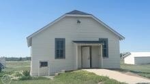 exterior of historic, white, one-room school house with blue sky and green grass