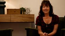 woman with brown short hair wearing short-sleeved burgundy red top smiling and sitting next to a desk
