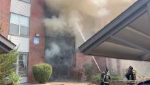 firefighters spraying water on smoke pouring out of a burning apartment building