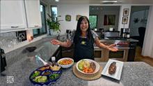 smiling Lindita wearing navy blue apron and showing off finished dish
