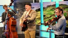 three men playing instruments, a cello, a guitar and a violin in front of a picture of a castle in Ireland