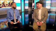 tv anchor and man wearing a hat sitting on stools and doing an interview