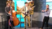 three men playing a cello, guitar and violin in front of an Irish cliffs image