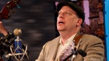 man wearing a flat hat and singing in front of a microphone